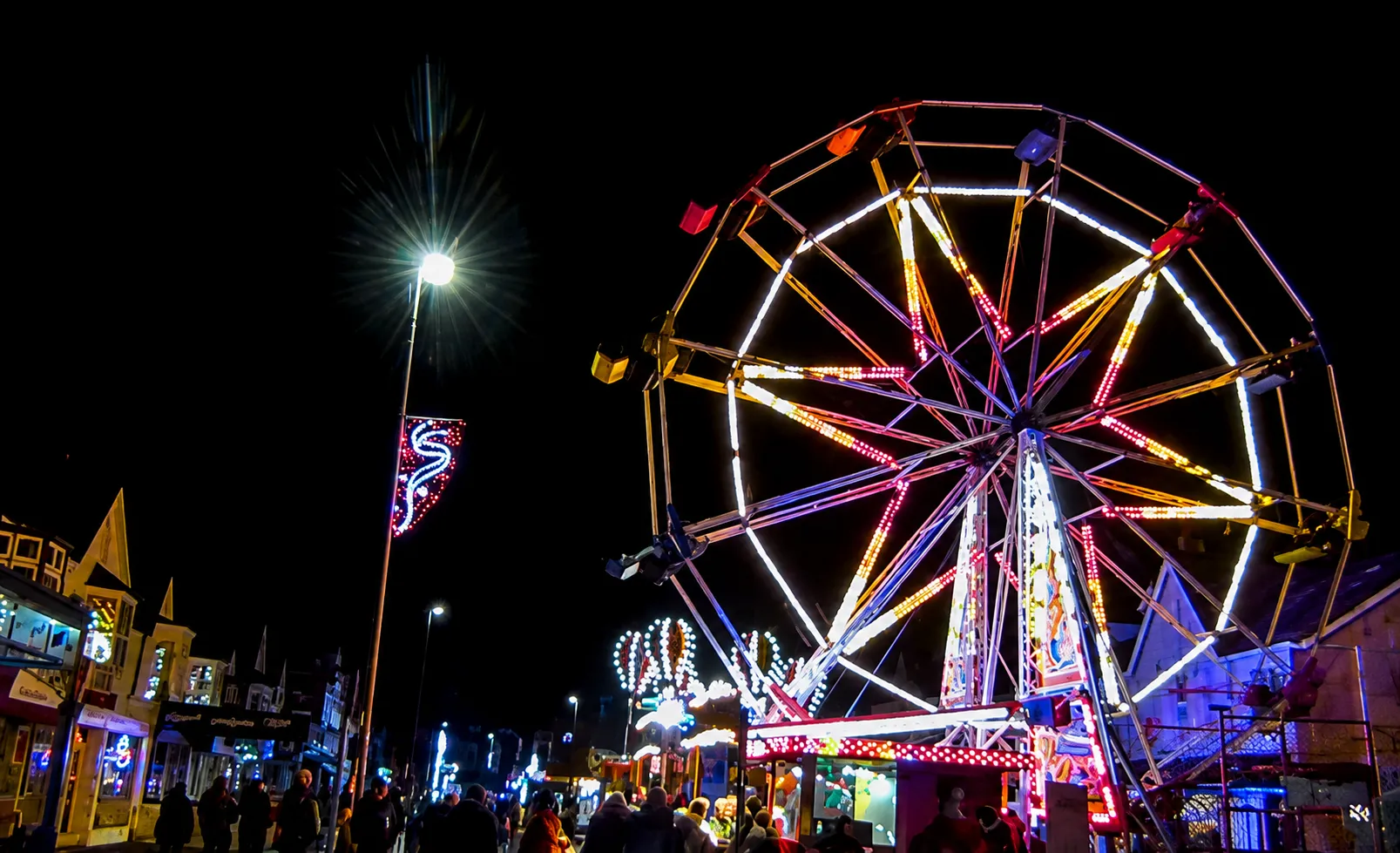 A ferris wheel lit up at night in bright colours of Purples and yellows